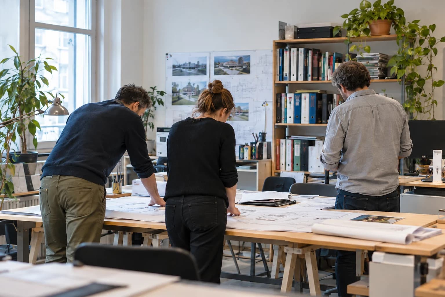 Trois personnes travaillent autour de plans dans un bureau d'études.